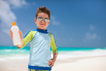 A child at the beach in a rash guard and sunglasses