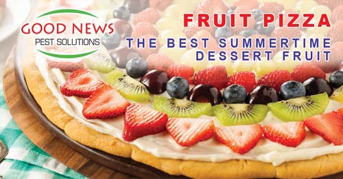 Fruit pizza atop a wooden platter, featuring toppings of strawberry, kiwi and blueberry